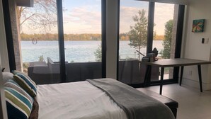 A bedroom with a bed, a desk, and a view of a lake.