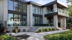 A modern multi-story house with large windows, a stone facade, and a landscaped front yard.