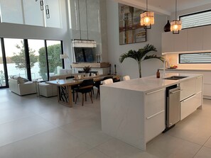 A modern kitchen with a central island, a dining area with a sofa, and a large window overlooking a body of water. - Chalet de luxe sur un lac-35 min de Toronto FIFA -les Muskokas à votre porte ! (Richmond Hill)