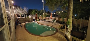 Ein Garten mit Swimmingpool, Liegestühlen und Lichterketten.