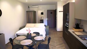 Hotelkamer met een bed, een eettafel met stoelen, een kitchenette en een badkamer op de achtergrond.