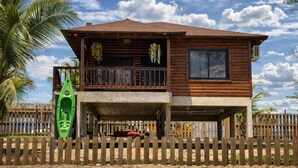 A two-story wooden building with a balcony, a covered area, and a fenced front. - Luxury cottage in front of the sea and lagoon of miami Tela (TELA)