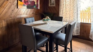 A dining area with a wooden table, four chairs, a hanging light fixture, and a painting on the wall. - Luxury cottage in front of the sea and lagoon of miami Tela (TELA)