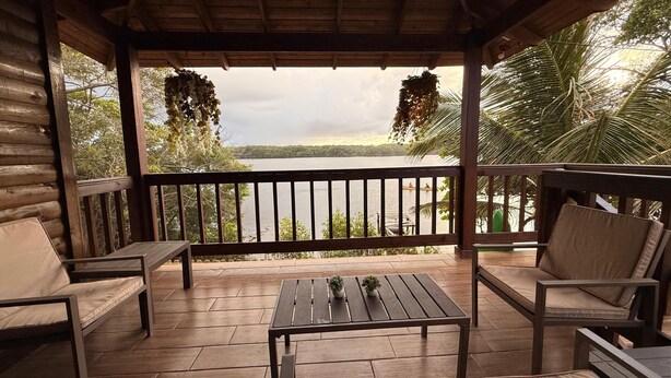 A wooden deck with a view of a lake, surrounded by palm trees and a wooden cabin. - Luxury cottage in front of the sea and lagoon of miami Tela (TELA)
