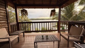 A wooden deck with a view of a lake, surrounded by palm trees and a wooden cabin. - Luxury cottage in front of the sea and lagoon of miami Tela (TELA)