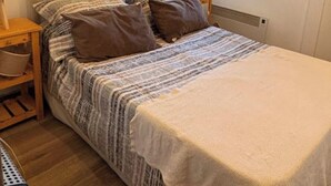 Ein Schlafzimmer mit Holzbalkendecke, einem Bett mit gemusterten Betttextilien, einem Nachttisch und einem Fenster.