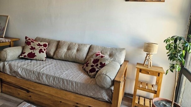 Ein gemütliches Zimmer mit einer Holzsofa, einem kleinen Holztisch, einer Lampe und einem Topfpflanze.