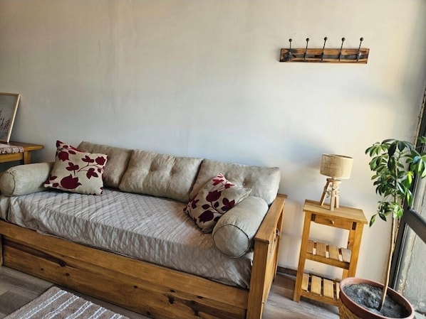 Una habitación acogedora con un sofá de madera, una mesita auxiliar de madera, una lámpara y una planta en maceta.