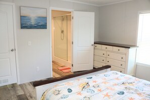 Un dormitorio con cama, cómoda, puerta que da a un baño y un cuadro en la pared.