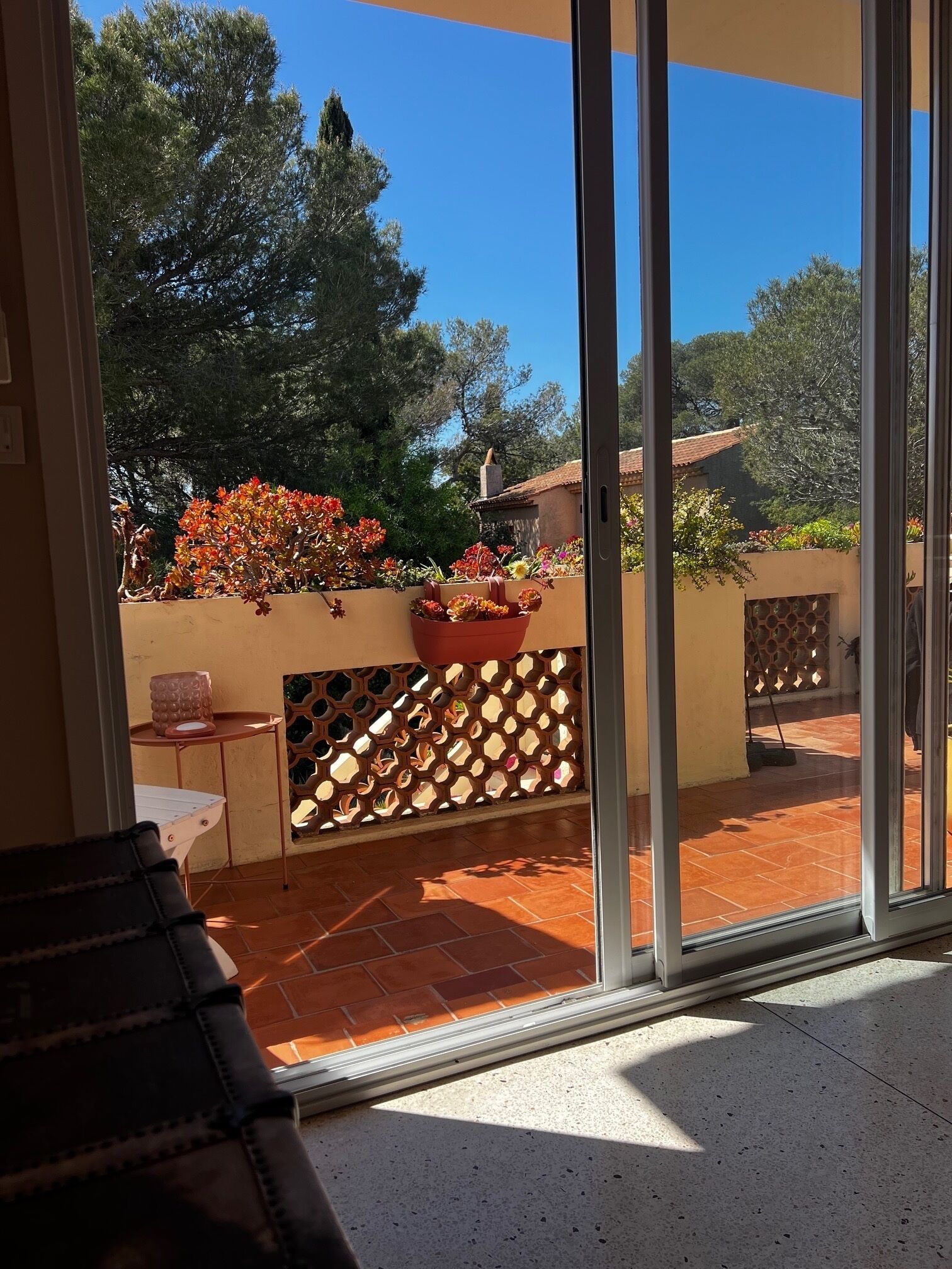 Habitació amb porta corredissa de vidre que dona a un pati exterior amb sòl de rajola, taula de fusta i una planta en test.