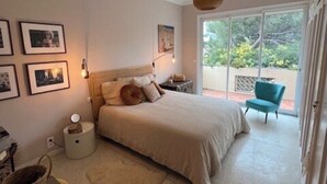 A bedroom with a bed, bedside tables, a chair, a small table, a basket, and a picture frame on the wall.