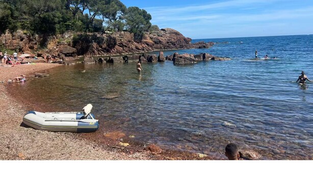 A beach with clear water, a boat, and rocky terrain.