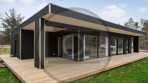 Una casa moderna con terraza de madera, amplios ventanales de vidrio y fachada oscura.