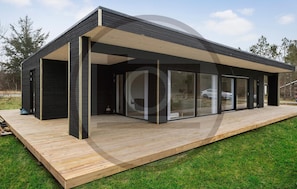 A modern house with a wooden deck, large glass windows, and a black exterior.