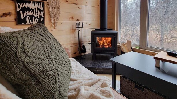 Interior acogedor de una cabaña con chimenea de leña, un ventanal grande y un letrero en la pared.