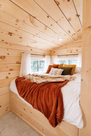 Ein Schlafzimmer mit Holzwänden, einem Bett, weißer Bettwäsche und einer braunen Decke.