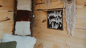 Interior de una cabaña de madera con una escalera, adornos de macramé en las paredes y un letrero motivacional.