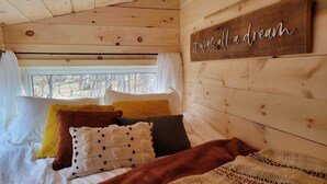 Un dormitorio de cabaña acogedor, con techo de madera, una cama con muchos almohadones, una ventana con cortinas y un letrero en la pared que dice 'it was all a dream'.