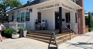 Ein Gebäude mit einem Schild, auf dem 'VILLAGE BAKING CO.' steht, mit einer Veranda und Stufen zum Eingang.