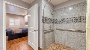 A bathroom with a shower, a door leading to a bedroom, and a window with blinds. - Lyfe Inn & Suites by AGA - Valley (Sun Valley)