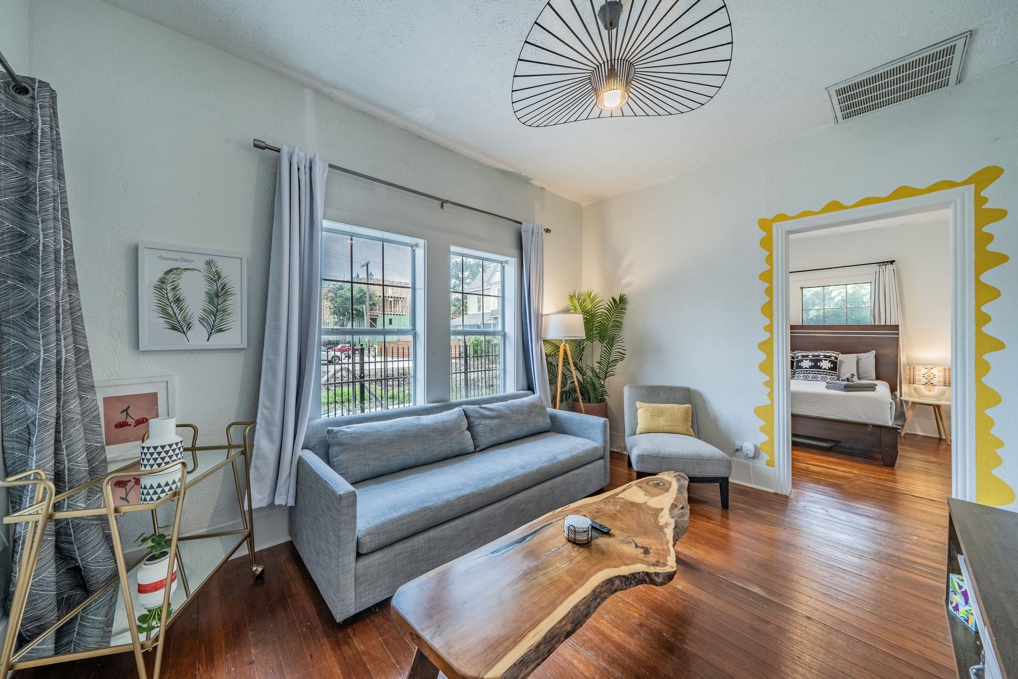 A modern living room with a grey sofa, a wooden coffee table, a small armchair, and a dining area with a bed.