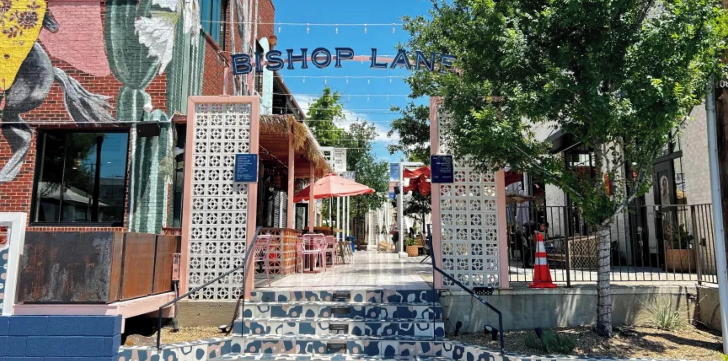 A street view with a sign reading 'Bishop Lane,' a brick building with a mural, and a patterned pavement.
