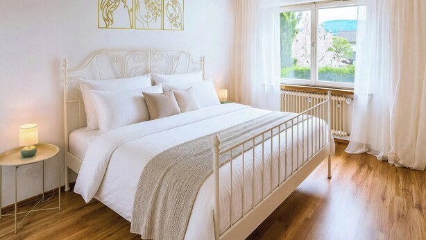 A bedroom with a bed, bedside tables, a window with curtains, a radiator, and wall art.