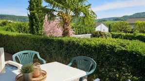 A patio with a table and chairs, surrounded by lush greenery and a view of a house in the distance.