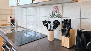 A kitchen with a stainless steel sink, a black countertop, wooden cabinets, and a range hood.