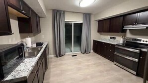 A kitchen with dark wooden cabinets, a granite countertop, a built-in oven, and a sliding glass door leading to a balcony. - University Hill Entire 5 BR House -  Walk to SU campus, Upstate Hospital (Syracuse)