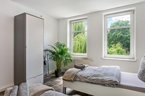 Un dormitorio con cama, una planta en maceta, un armario y una ventana con vistas a follaje verde.