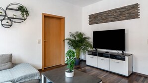 A modern living room with a sofa, a coffee table, a TV, a cabinet, and a door. - [G2] Apartment for 6 People (75m²) in Gera (Gera)