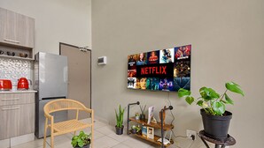 A modern kitchen with a refrigerator, a wooden chair, a potted plant, and a wall-mounted TV displaying Netflix content. - Lofthaus Rosebank: walk to mall, safe & central. Family friendly 2BR with WIFI (Johannesburg)