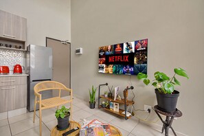 Eine moderne Küche mit Kühlschrank, einem Holzstuhl, einer Topfpflanze und einem an der Wand montierten Fernseher, der Netflix-Inhalte zeigt.