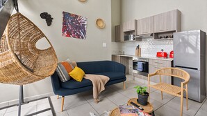 A modern living room with a sofa, a hanging chair, and a dining area with a table and chairs. - Lofthaus Rosebank: walk to mall, safe & central. Family friendly 2BR with WIFI (Johannesburg)
