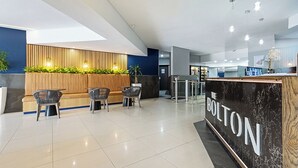 A modern reception area with a wooden reception desk, seating area, and a plant wall. - Lofthaus Rosebank: walk to mall, safe & central. Family friendly 2BR with WIFI (Johannesburg)