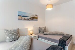 A bedroom with two beds, a nightstand, a lamp, and a beach-themed painting on the wall. - [G1] Apartment for 4 People (55 m²) in Gera (Gera)