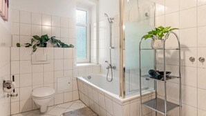 Une salle de bain moderne équipée d’une baignoire, d’une douche, de toilettes et d’une étagère en verre où est placée une plante.