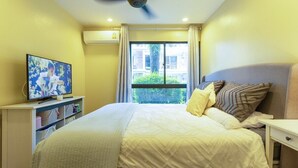 Een slaapkamer met een bed, een televisie, een plafondventilator en een raam met gordijnen.