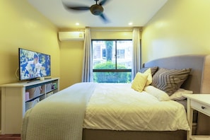 Ein Schlafzimmer mit Bett, Fernseher, Deckenventilator und einem Fenster mit Vorhängen.