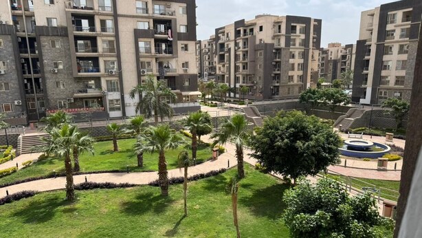 Un complesso residenziale con diversi edifici, una zona verde centrale con palme e una fontana circolare.
