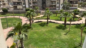 Un edificio residenziale con diversi balconi, un giardino curato con palme e un cielo sereno.