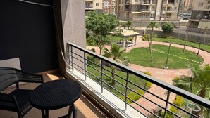 Un balcone con due sedie e un tavolo, affacciato su un cortile curato con un gazebo e palme.