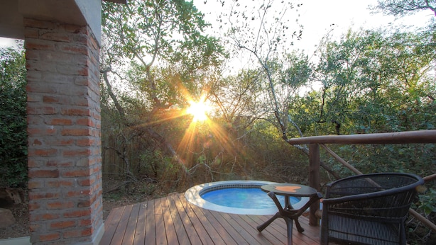 Una terraza de madera con un jacuzzi, rodeada de árboles y un muro de ladrillo.