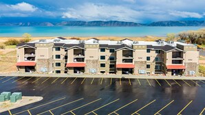 A multi-story hotel with a parking lot in front, surrounded by mountains and a lake. - Water's Edge 102 | Bear Lake Views| Lakeside Unit (Garden City)