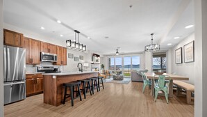 A modern kitchen with wooden cabinets, stainless steel appliances, and a central island with stools. - Water's Edge 102 | Bear Lake Views| Lakeside Unit (Garden City)