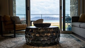 A living room with a view of the beach, a wicker chair, a leather armchair, and a textured coffee table. - Water's Edge 102 | Bear Lake Views| Lakeside Unit (Garden City)