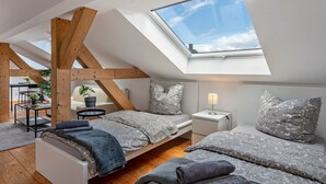 Quarto estilo loft com claraboia, duas camas, escrivaninha e uma cadeira.