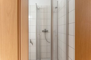 Une douche avec une porte en verre, des murs recouverts de carreaux blancs et un robinet en métal.