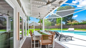 Un patio techado con una mesa y sillas de comedor, una piscina y vistas a un jardín trasero.